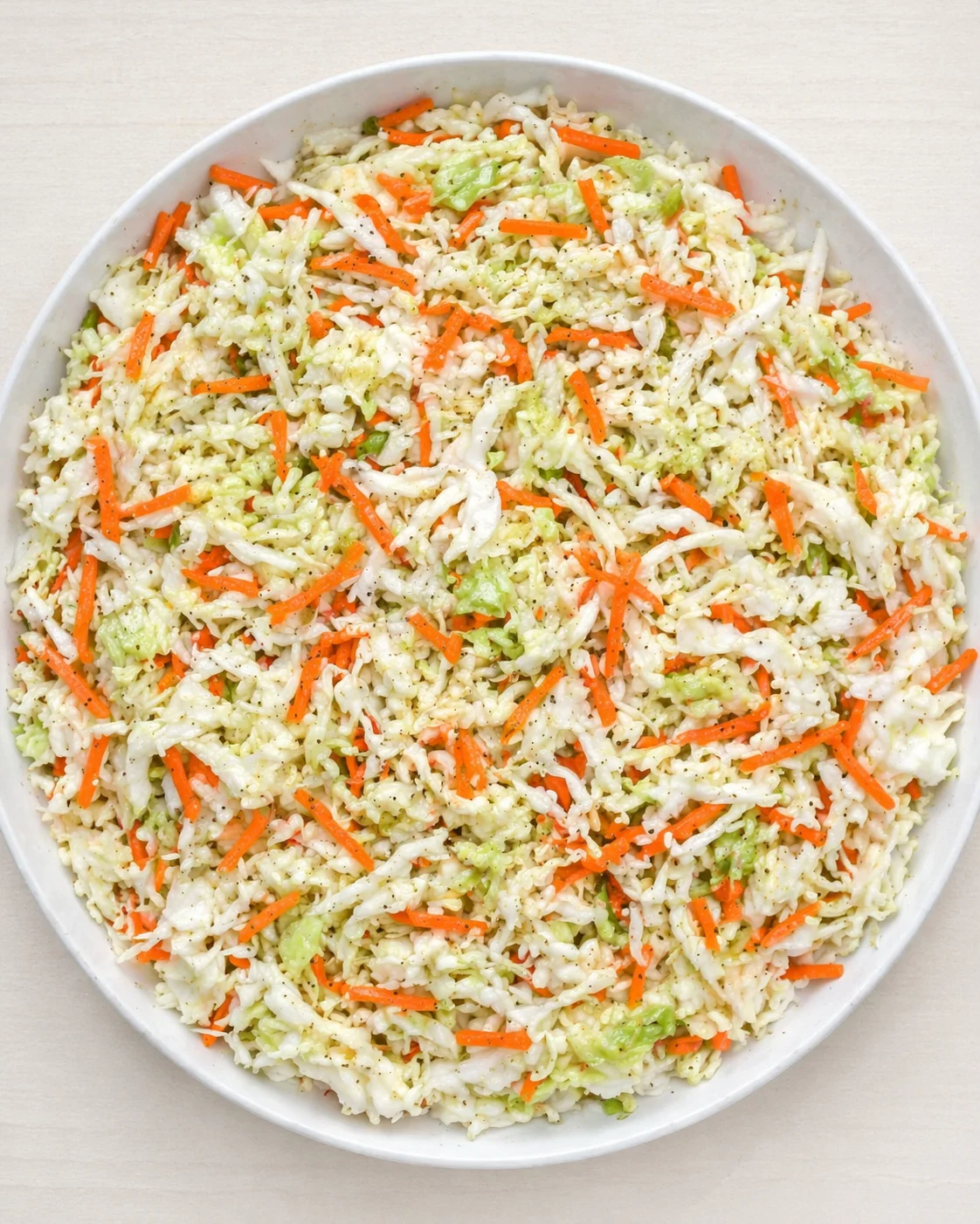 top-down view of a round white dish filled with shredded cabbage, carrot sticks, and fried rice.