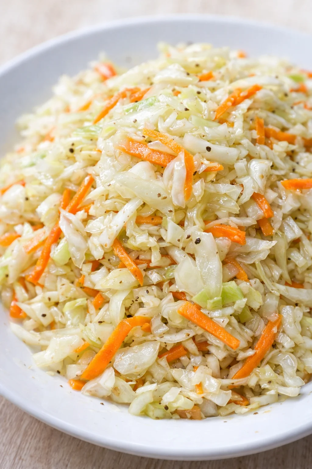 pile of shredded cabbage and orange carrot slaw in a light blue bowl on a wooden surface