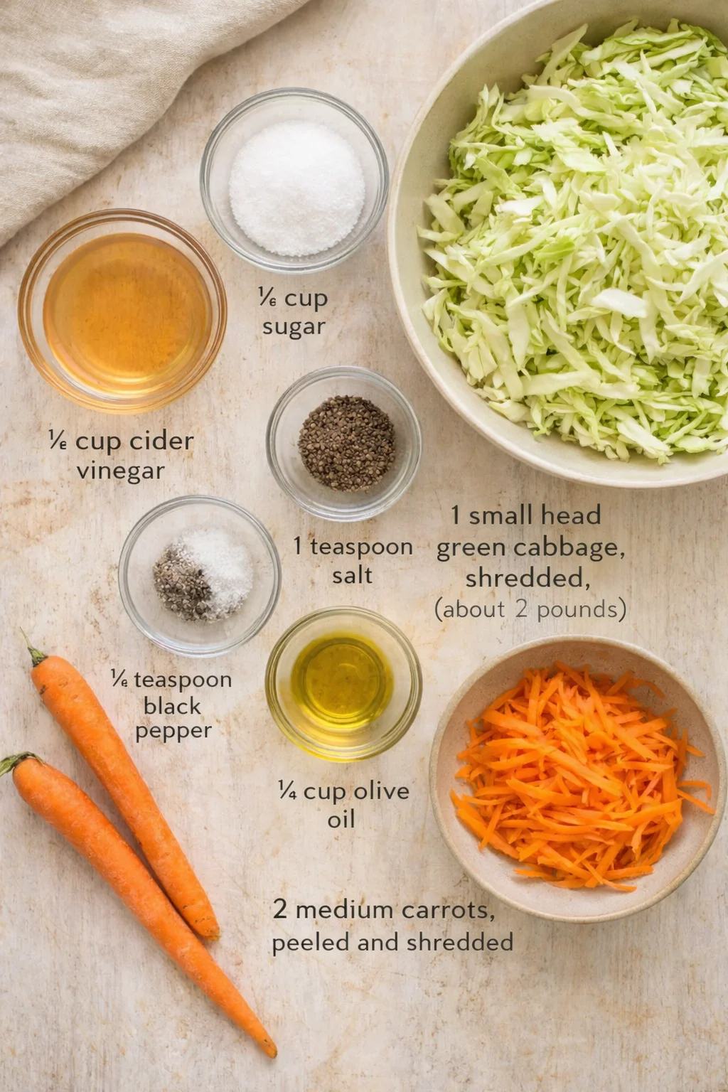Top-down view of shredded cabbage and carrots with labeled bowls of sugar, vinegar, oil, salt, and pepper.