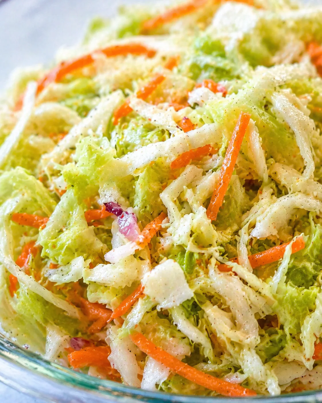 Close-up of creamy shredded cabbage and carrot slaw in a glass bowl.