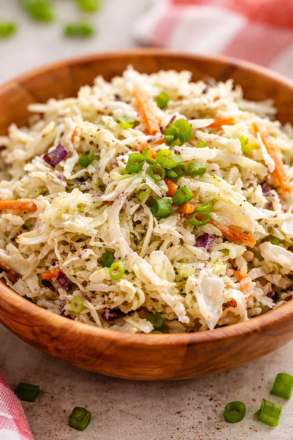 Shredded cabbage coleslaw with carrots and green onions in a wooden bowl