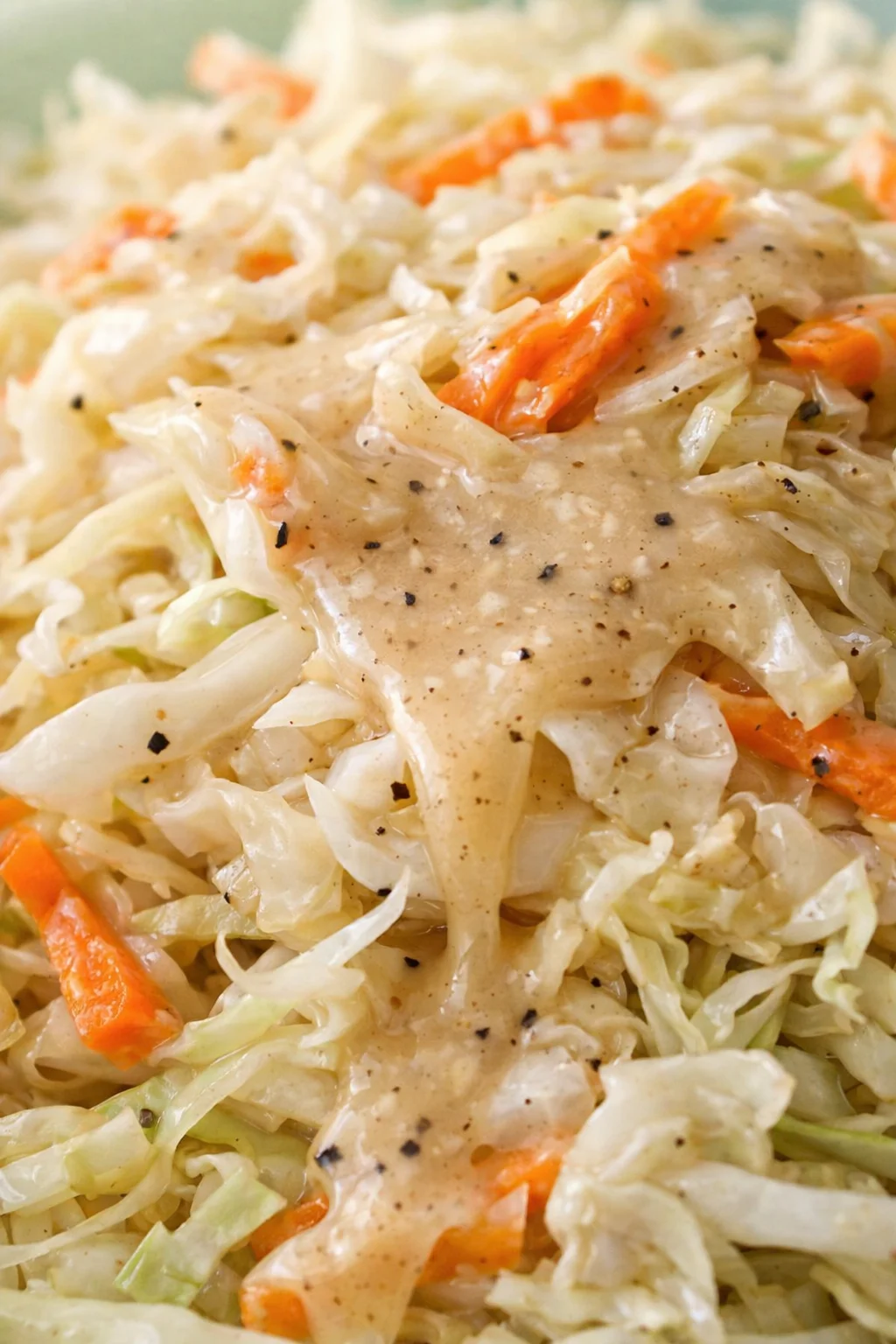 Close-up of shredded cabbage and carrot slaw in a creamy dressing, speckled with black pepper.
