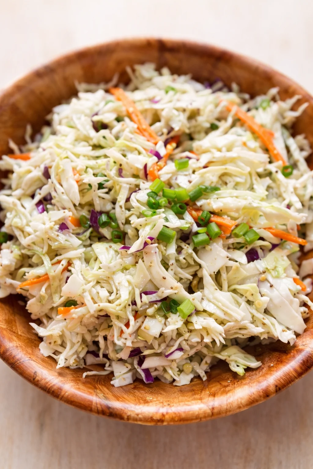 Wooden bowl of creamy coleslaw with shredded cabbage, carrots, purple cabbage, and green onions