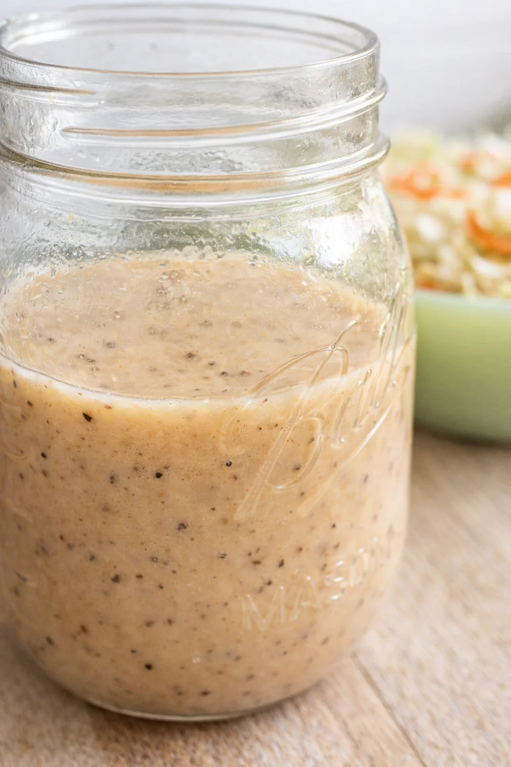 Close-up of a speckled creamy dressing in a mason jar on a wooden table.