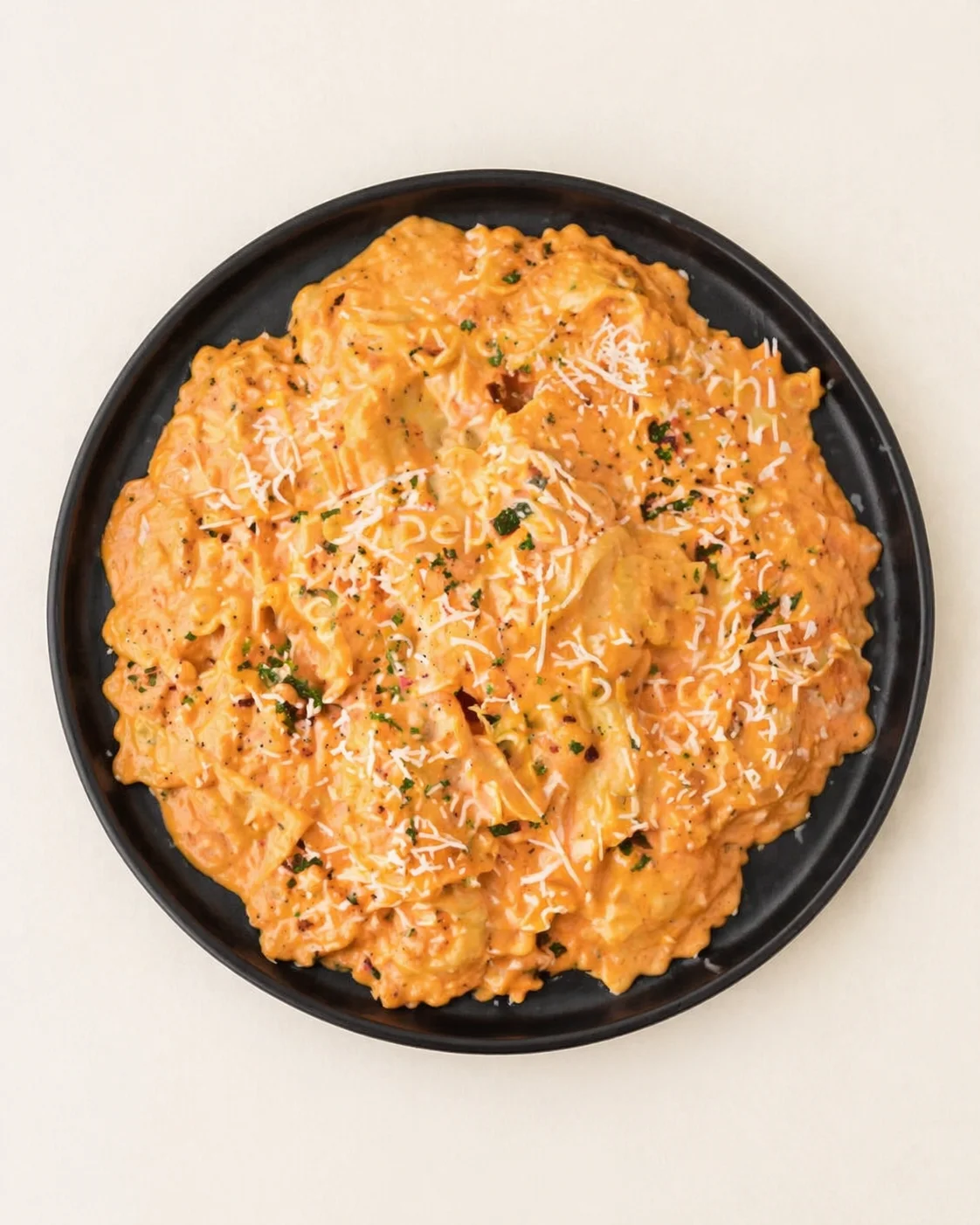 top-down view of creamy orange tomato pasta on a black plate sprinkled with cheese and herbs