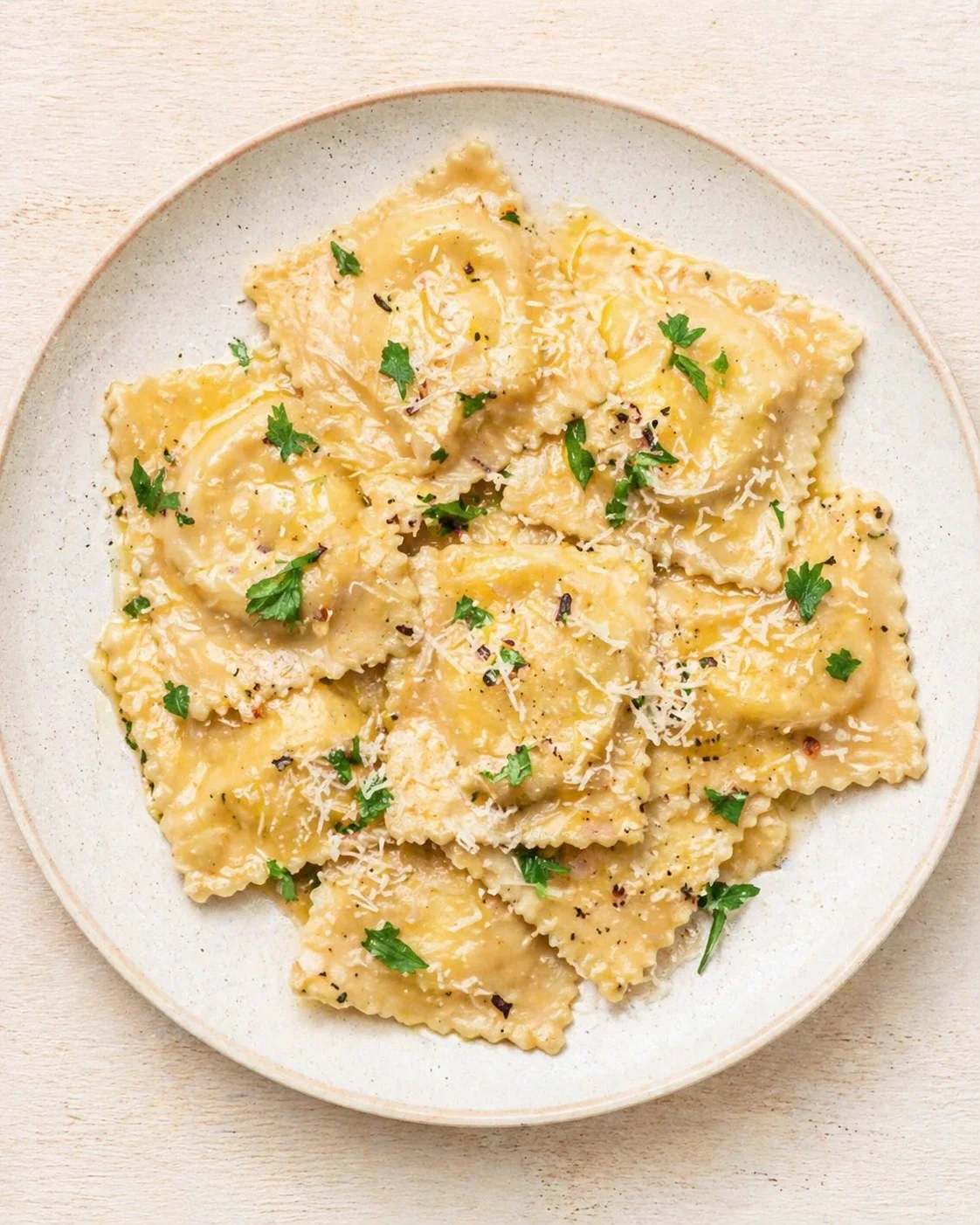 plate of creamy ravioli sprinkled with parmesan and parsley on a light wooden surface