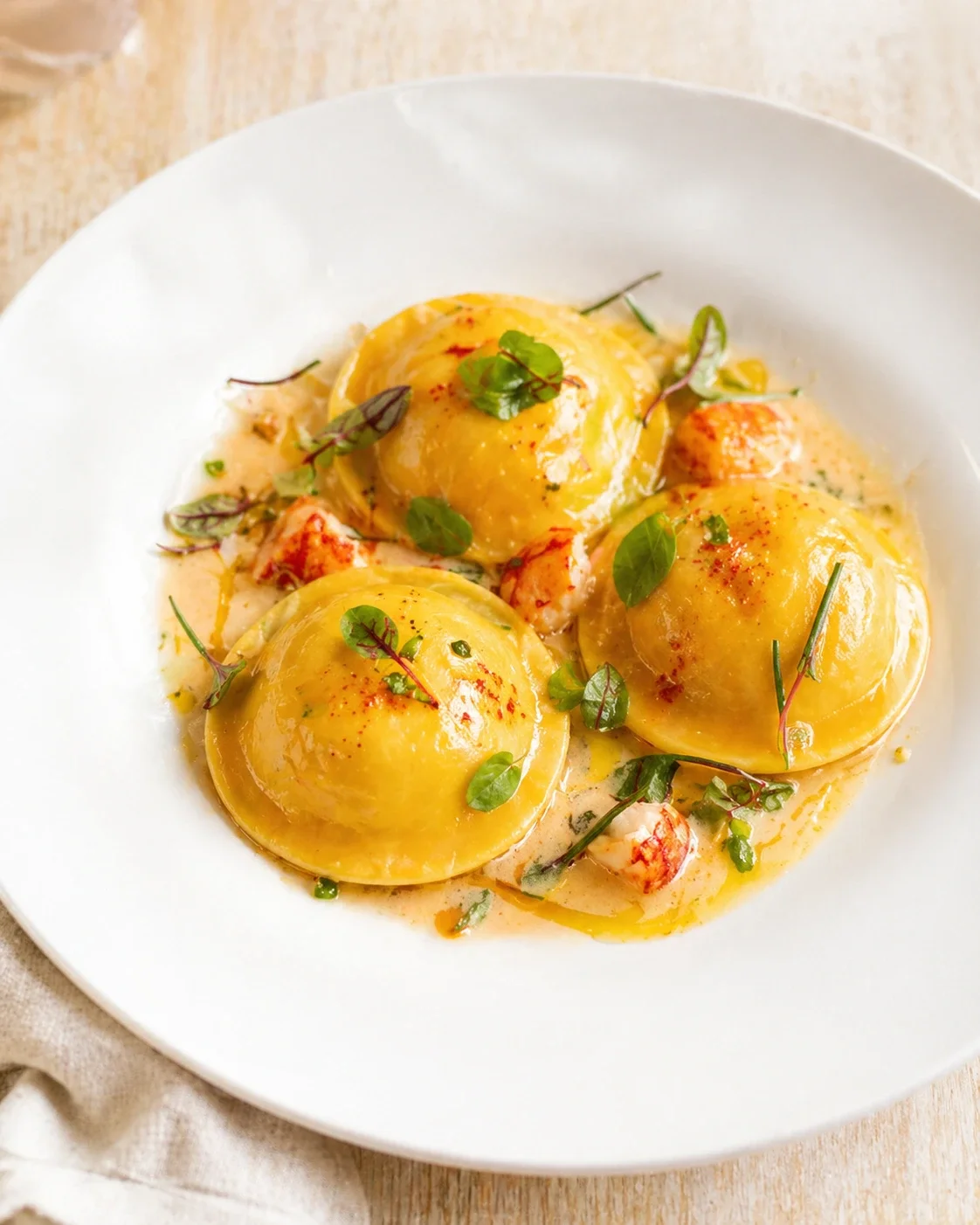 Plated golden ravioli in orange cream sauce with greens and herbs