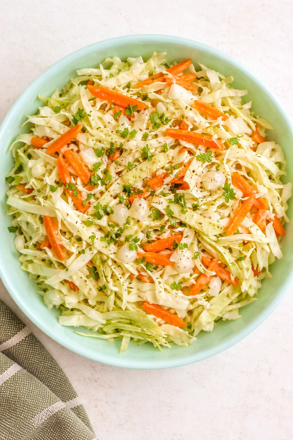Overhead view of creamy coleslaw with shredded cabbage, carrot strips, and parsley in a mint-green bowl.
