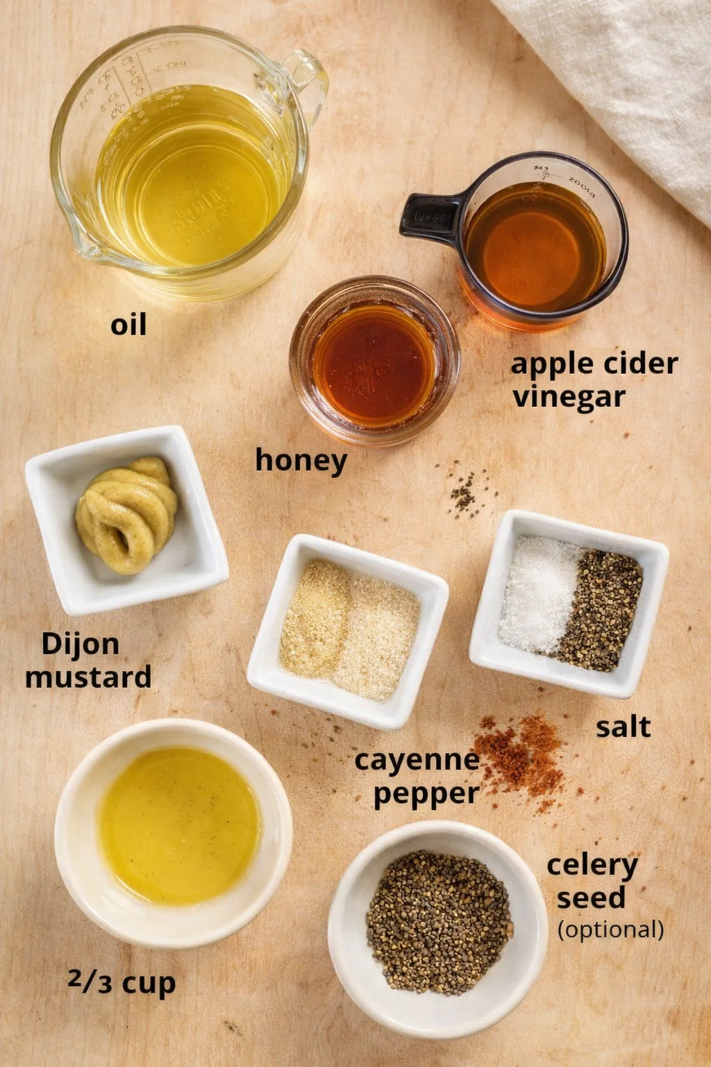 top-down view of oil, honey, apple cider vinegar, Dijon mustard, salt, pepper, and spices on a wooden board