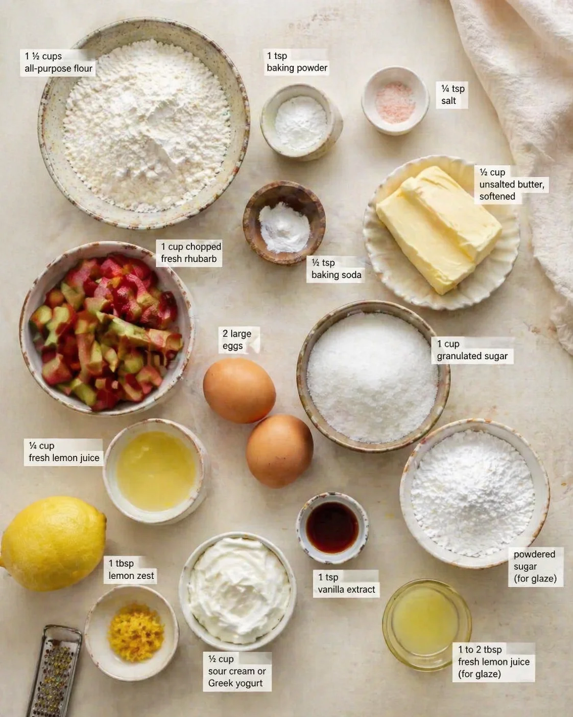 Overhead view of flour, rhubarb, eggs, lemon and dairy ingredients arranged for lemon yogurt rhubarb cake.