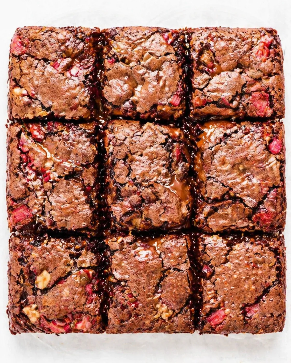 top-down view of fudgy brownie slab studded with raspberry chunks, cut into squares on white parchment.