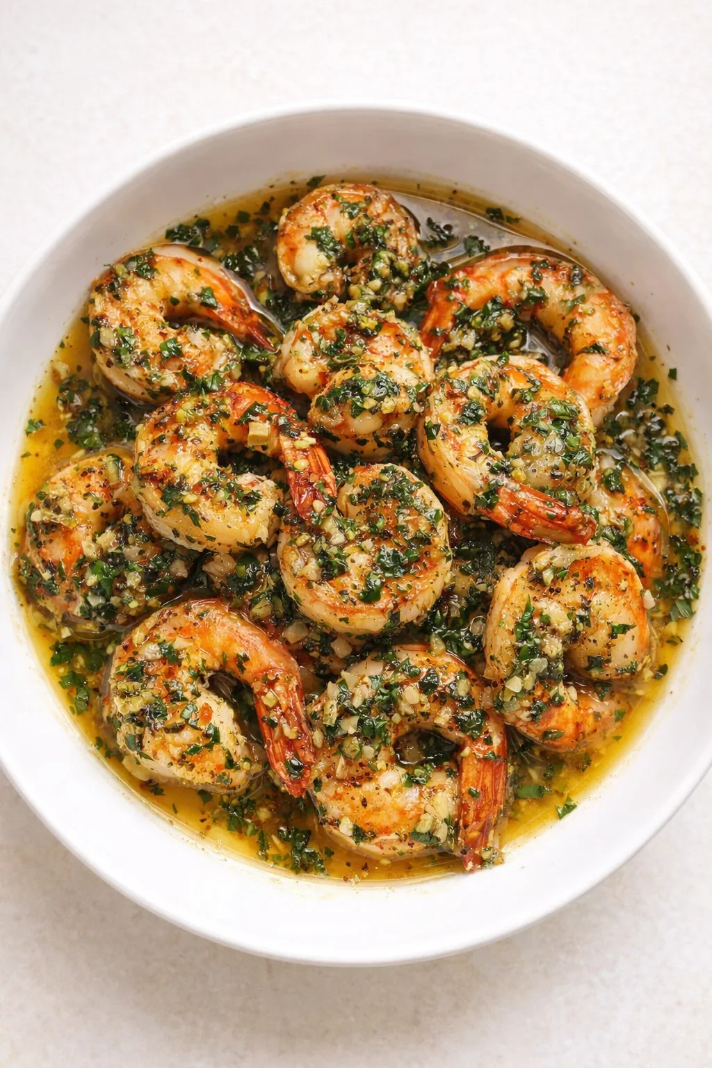 plump shrimp coated in garlic-parsley butter sauce in a white bowl.
