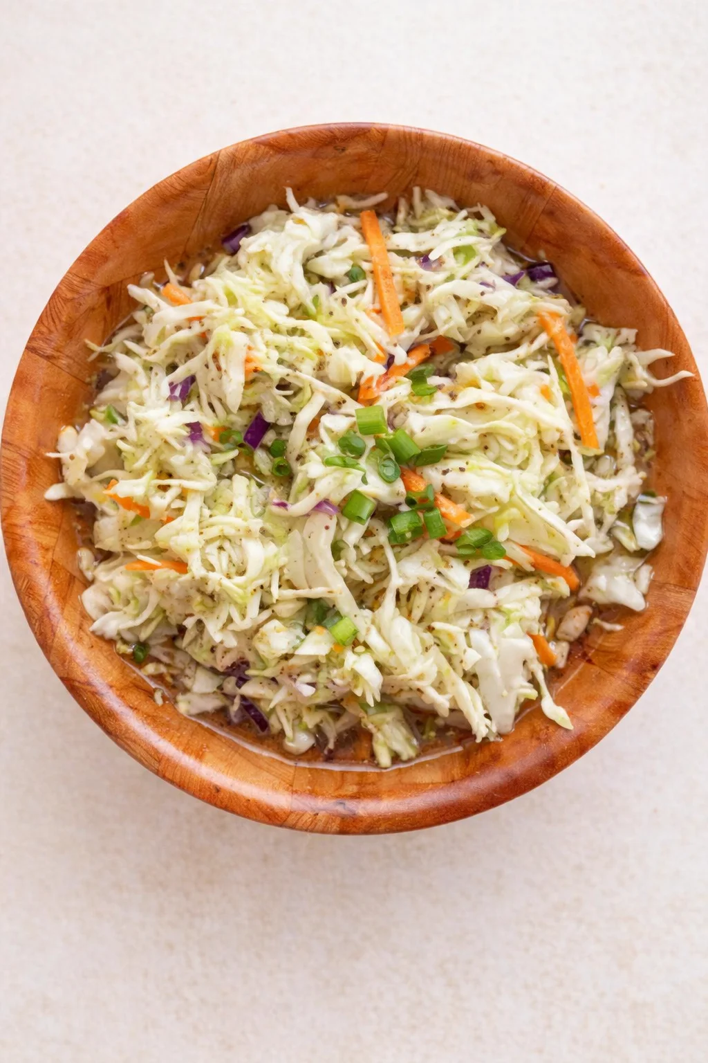 Shredded cabbage coleslaw with carrot, purple onion, and green onion in a wooden bowl.