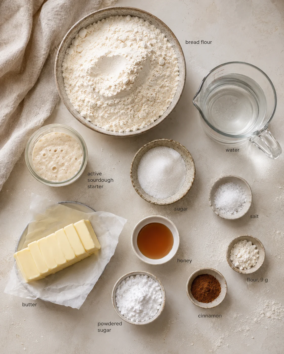 assorted baking ingredients laid out on a beige counter, including flour, water, butter, and sugar