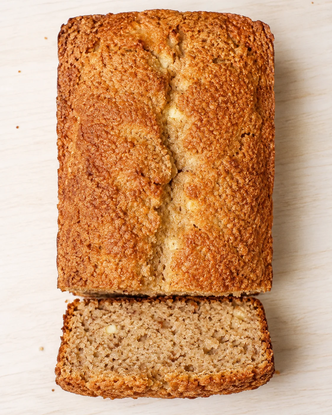 Golden banana bread loaf with crusty top, sliced to show tender crumb on a light wooden board