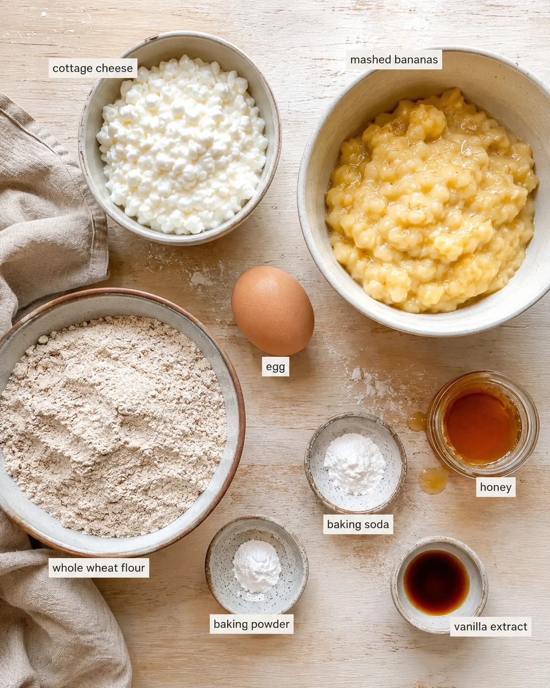 Top-down view of baking ingredients laid out on a wooden surface with labeled bowls.