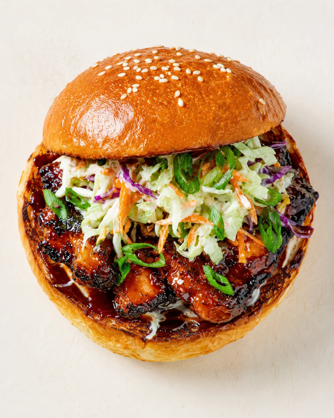 glossy sesame-bun burger with sticky glaze, creamy slaw, and green onion garnish