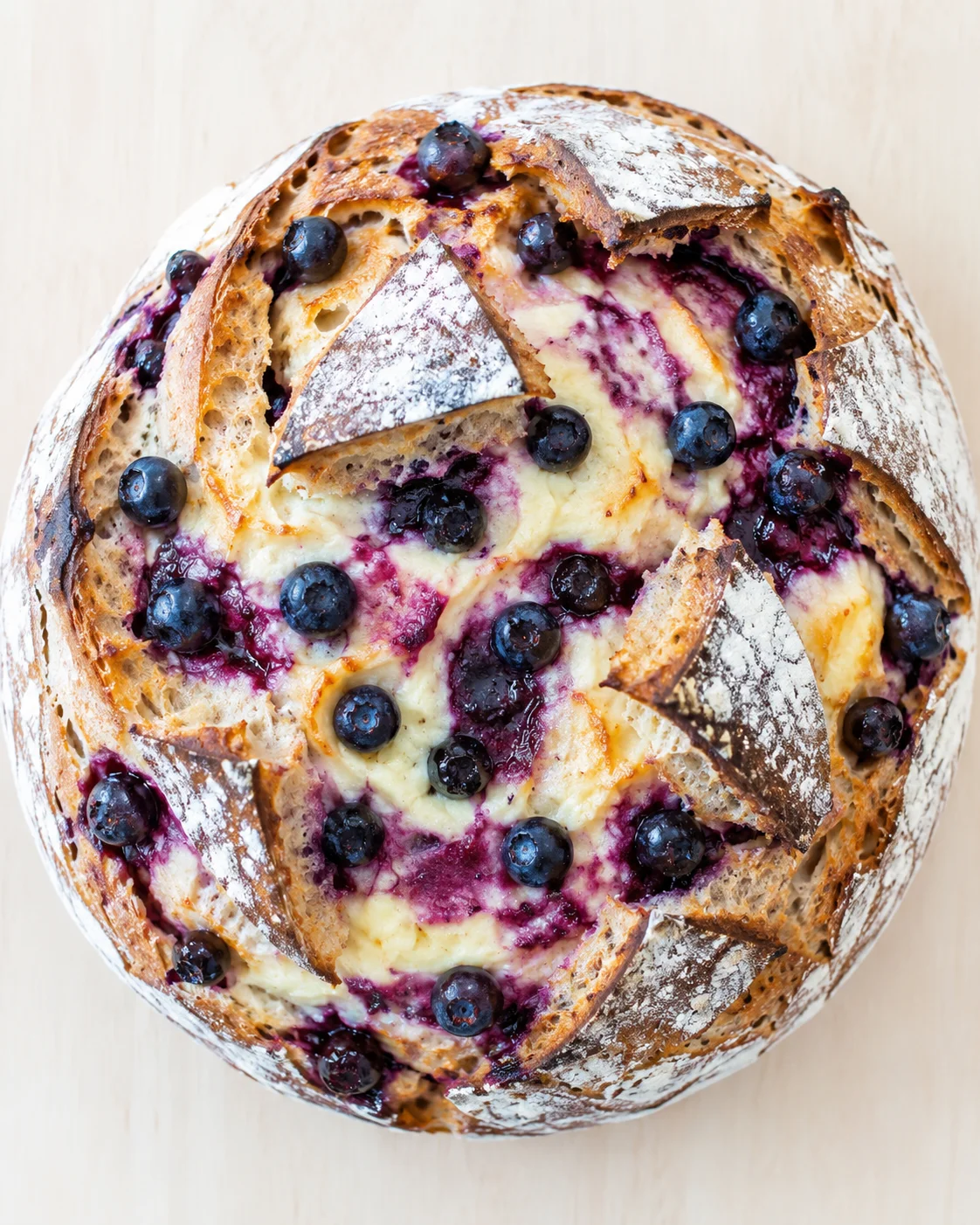 Round rustic loaf with flour-dusted crust, blueberry filling, and creamy cheese center
