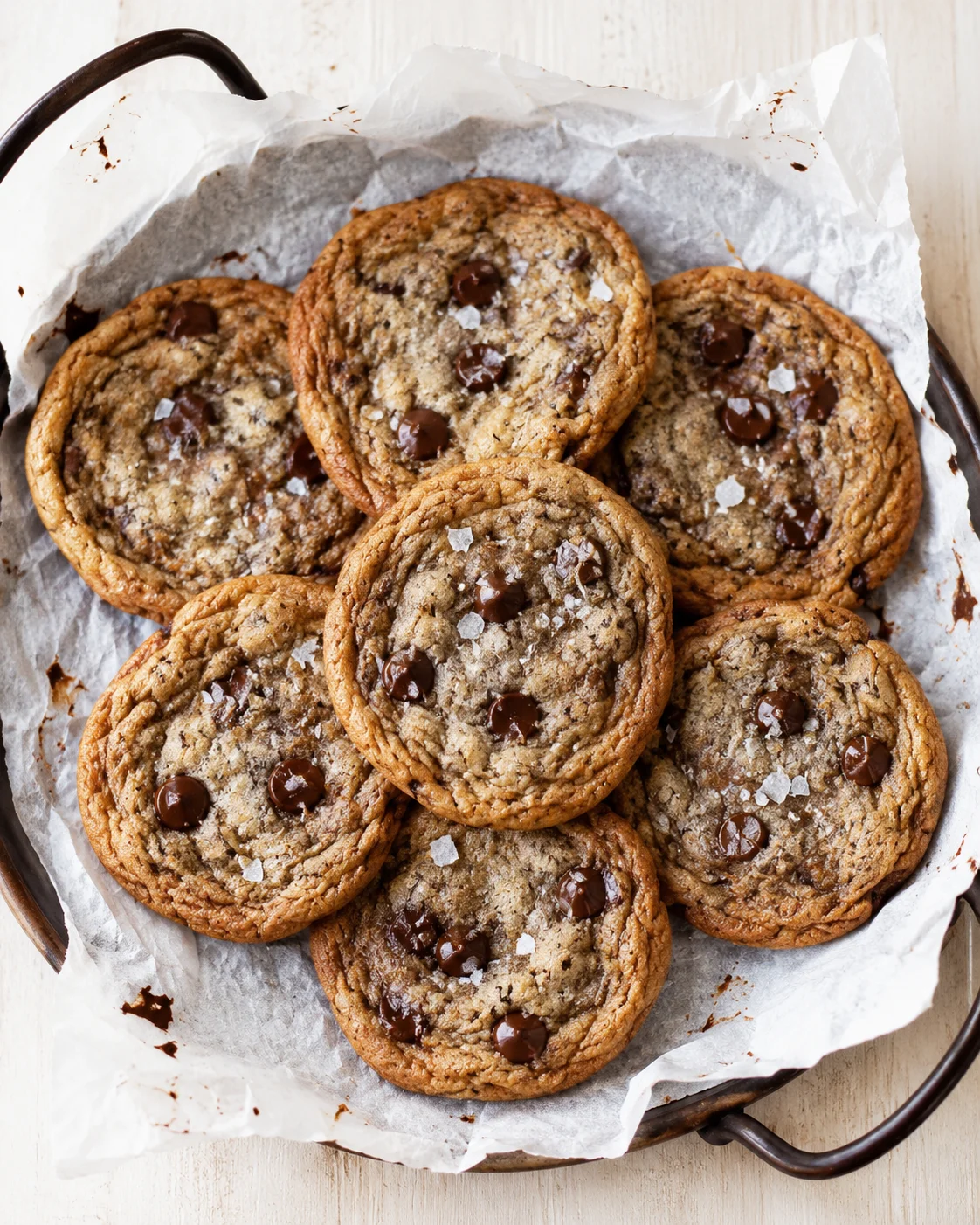 Overhead view of a round skillet lined with parchment, piled with chocolate chip cookies.