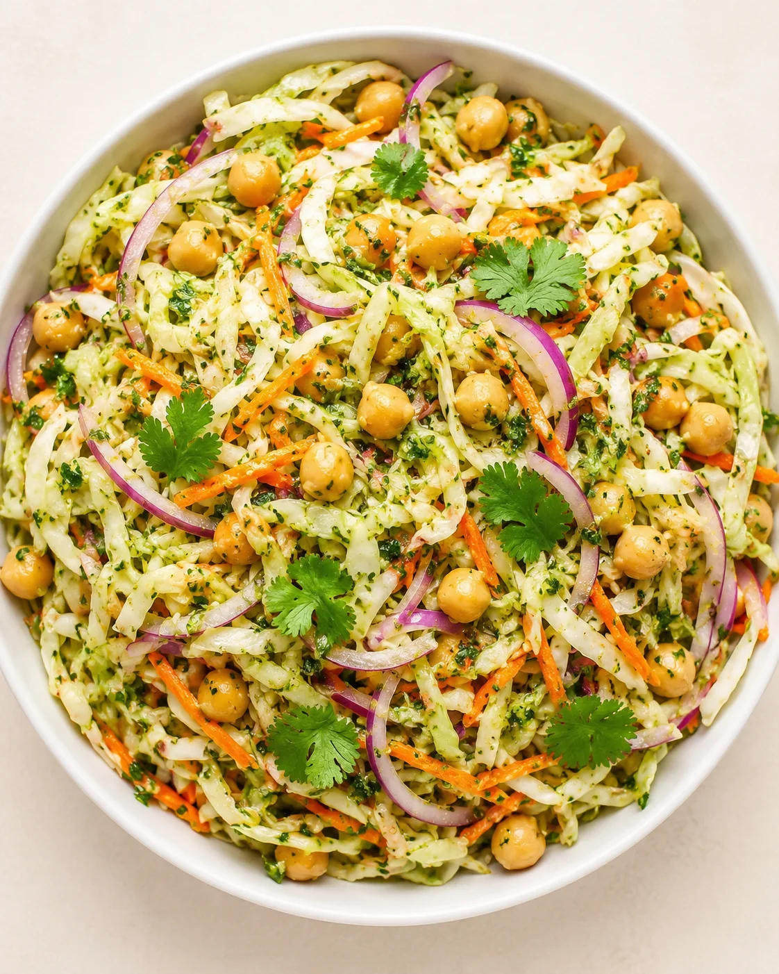 Top-down view of a white bowl filled with chickpea and shredded cabbage salad, garnished with red onion, carrot, and cilantro.