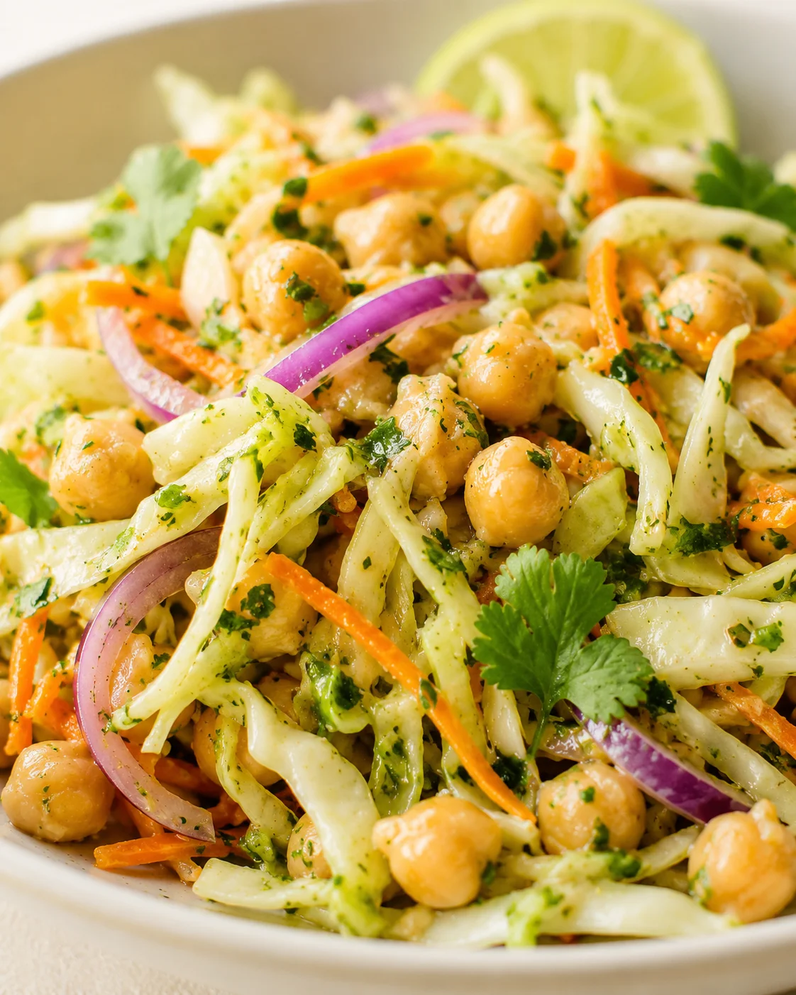 Close-up of a colorful chickpea salad with shredded cabbage, carrots, red onions, cilantro, and lime.