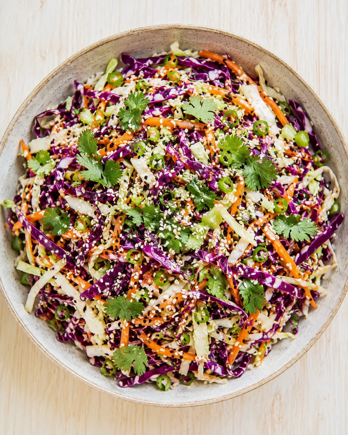 Round ceramic bowl filled with vibrant slaw: purple cabbage, carrot ribbons, green onion, cilantro, sesame seeds.