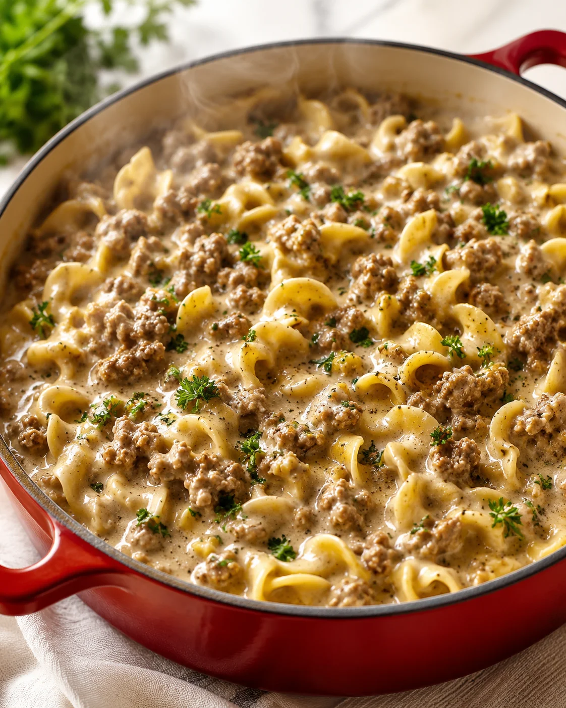 red skillet filled with creamy beef and noodles, garnished with parsley