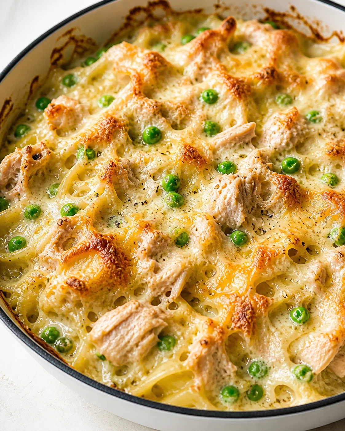 Creamy chicken and pasta bake with green peas in a white skillet