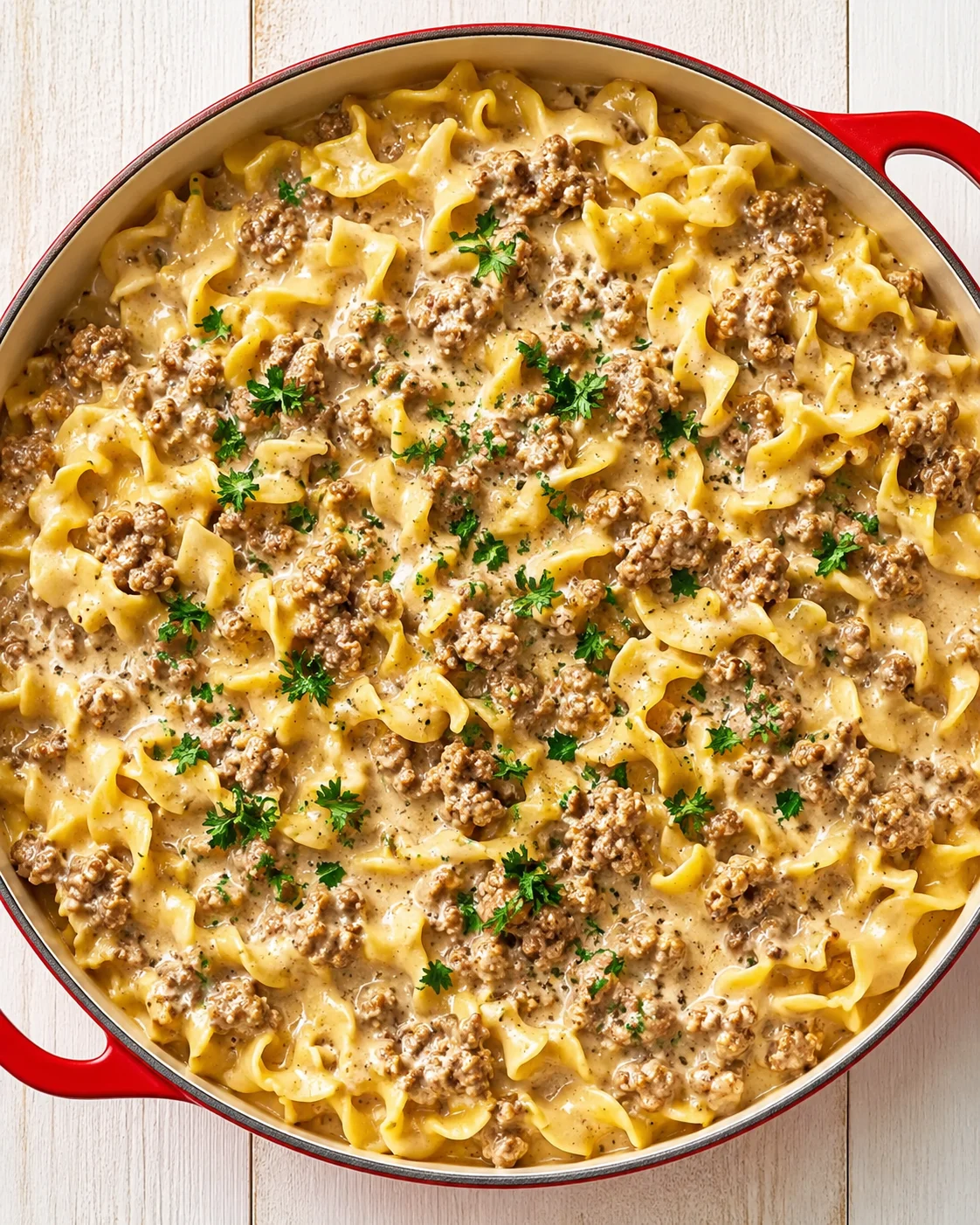 Creamy beef pasta with wide ribbon noodles and herbs in a red skillet