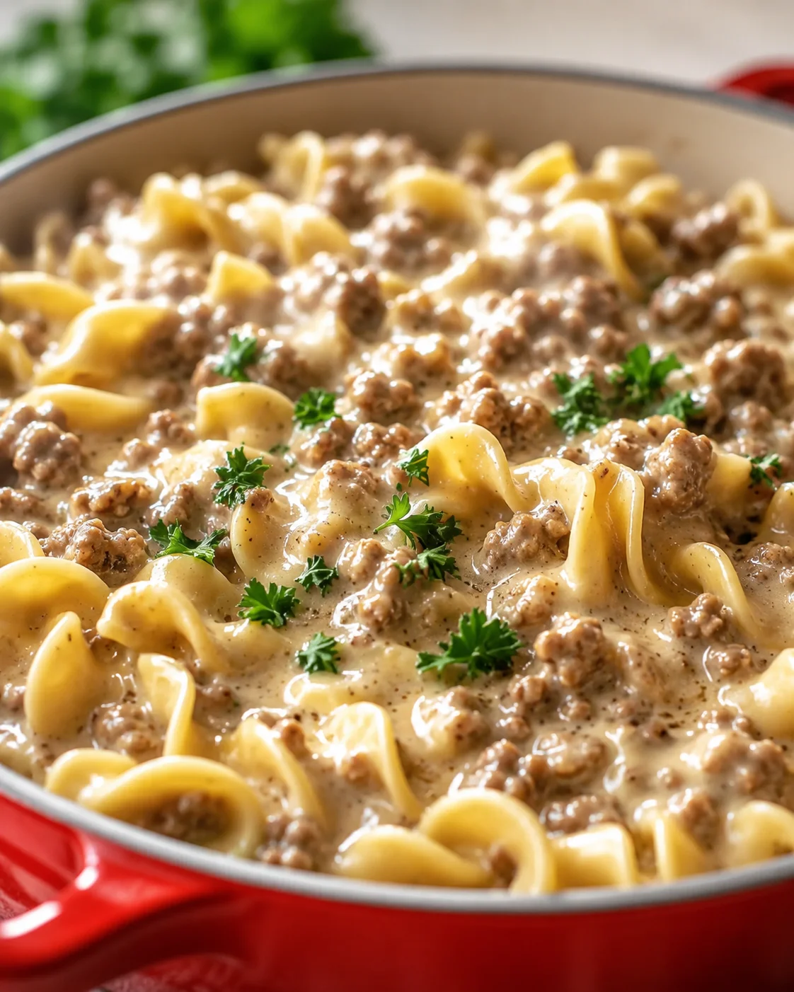 Close-up of creamy meat sauce pasta in a red skillet, garnished with parsley