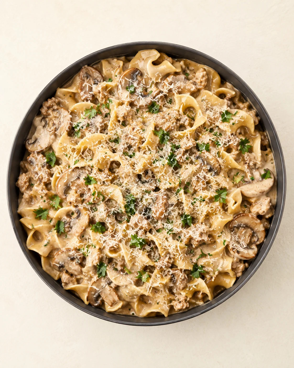 top-down view of creamy mushroom pasta in a dark bowl, topped with parmesan and parsley
