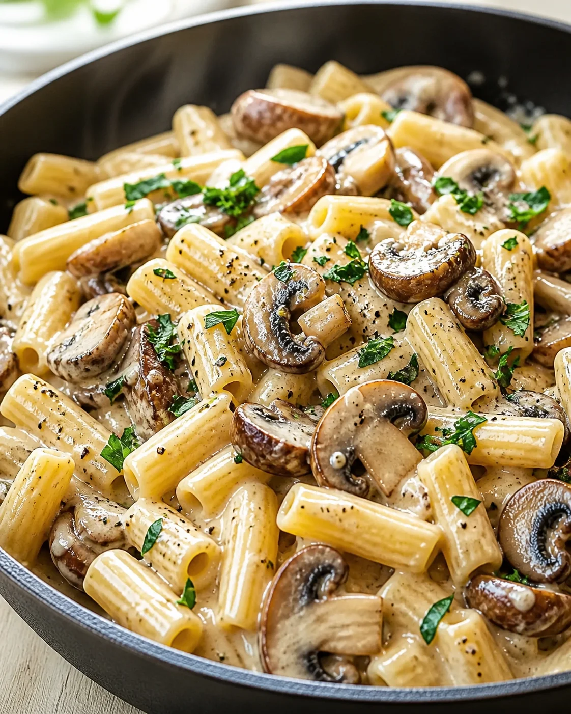 Creamy mushroom pasta with rigatoni, sautéed mushrooms, and chopped parsley in a skillet with glossy sauce.