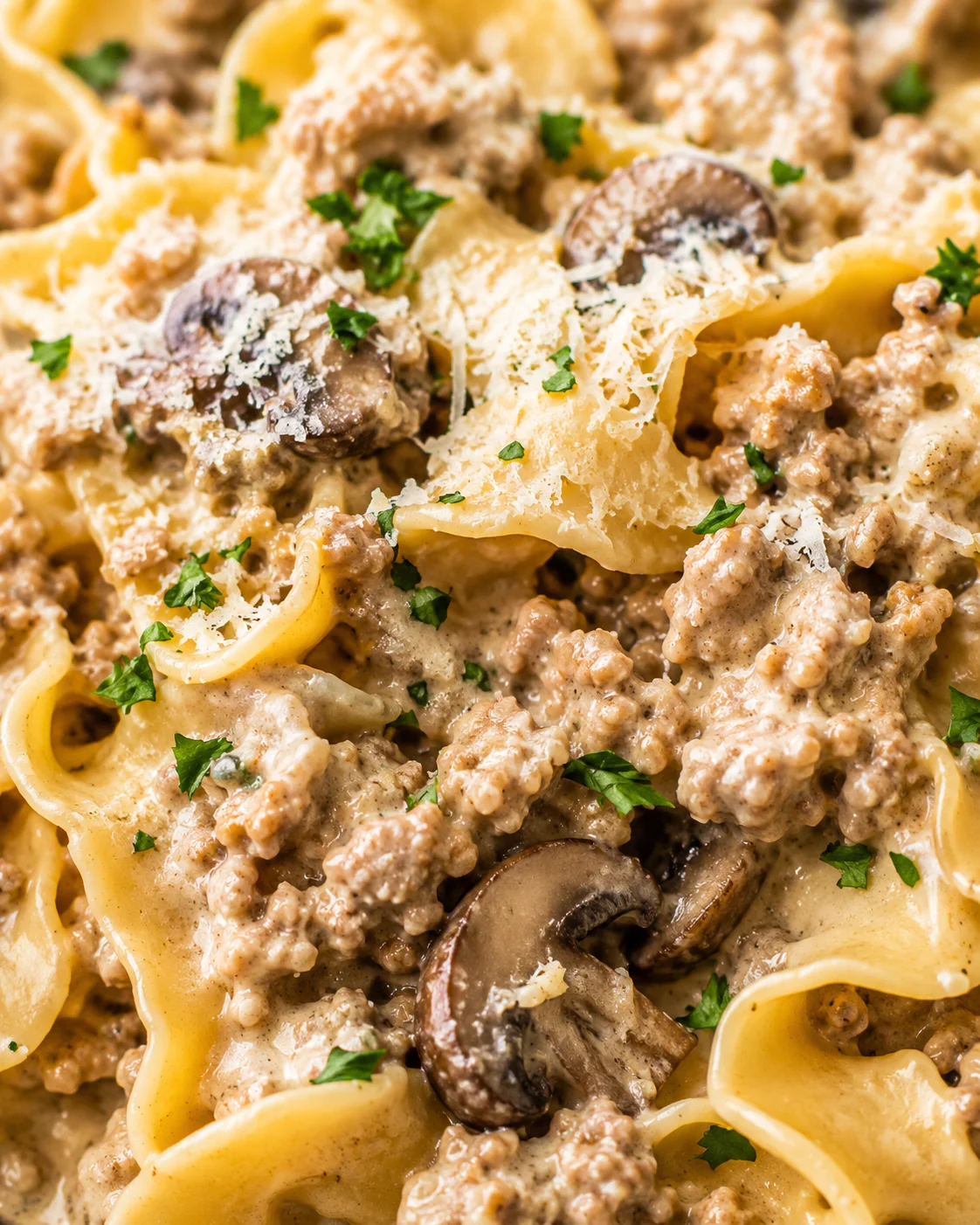 Close-up view of creamy pasta with ground meat, mushrooms, parmesan, and chopped parsley.
