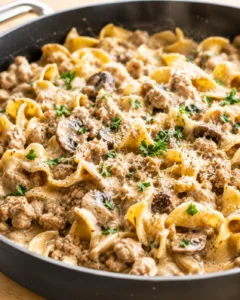 Close-up of creamy sausage and mushroom pasta in a black skillet, garnished with parsley.