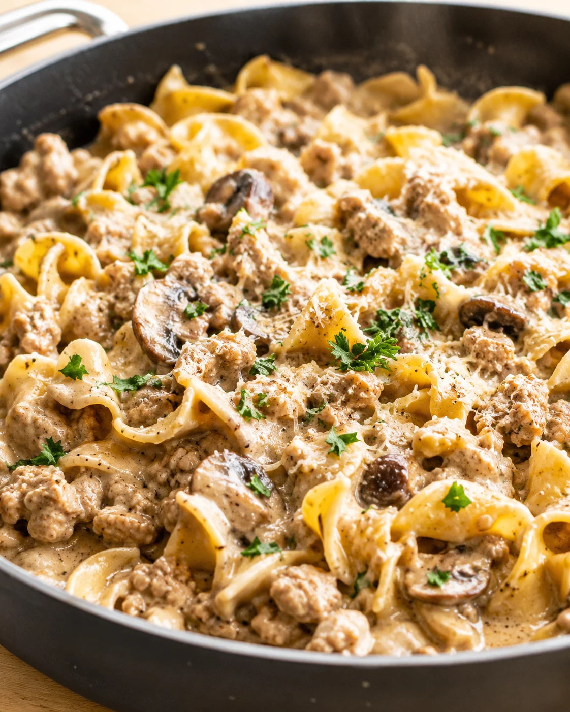 Close-up of creamy sausage and mushroom pasta in a black skillet, garnished with parsley.