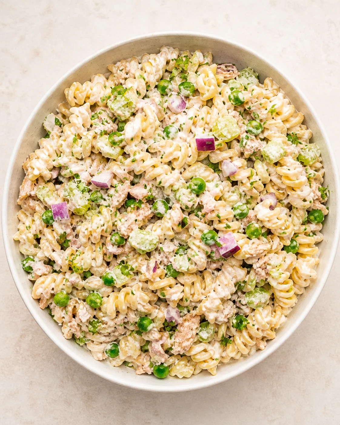 round bowl of creamy pasta salad with fusilli, peas, red onion, avocado, and herbs
