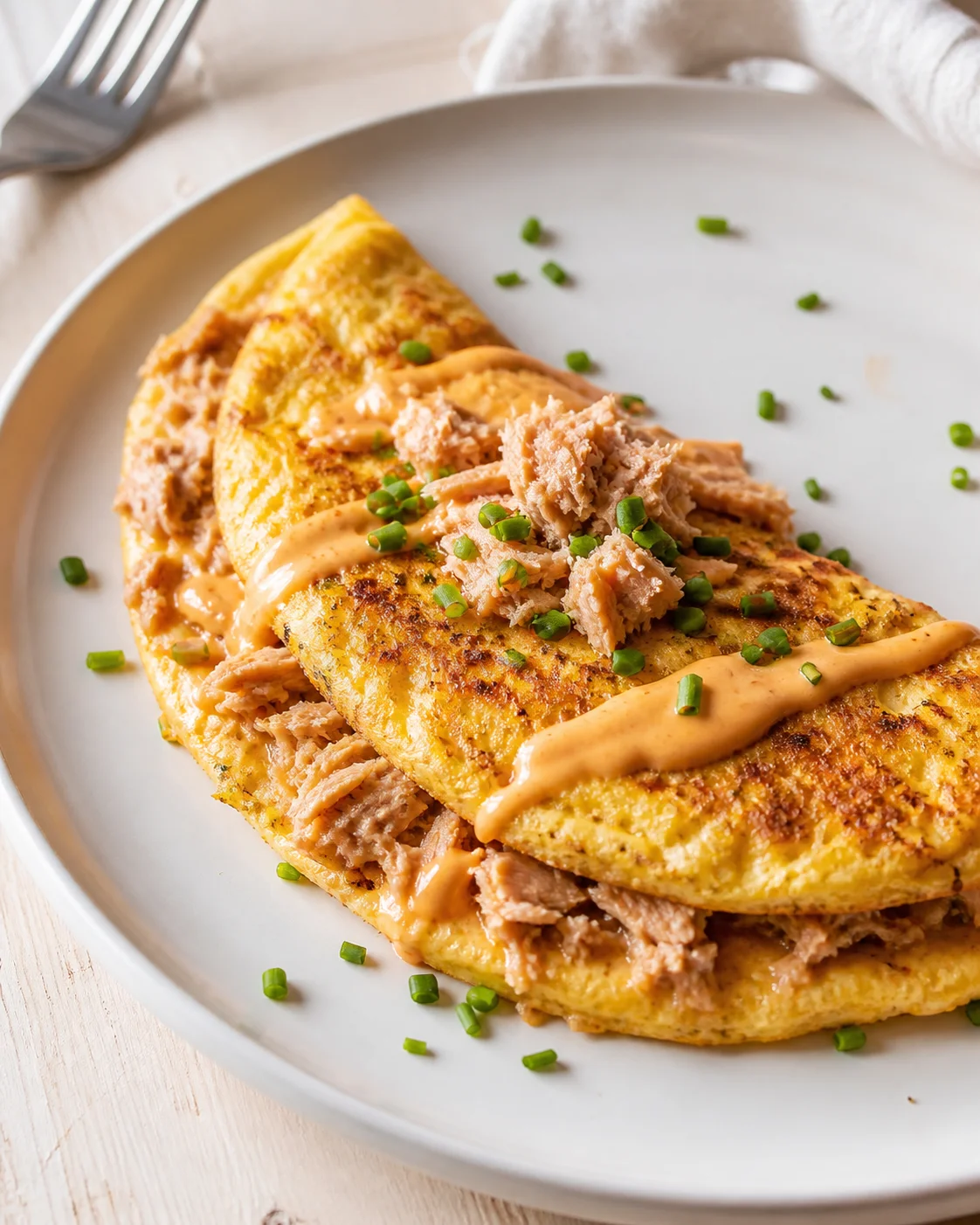 two golden-brown crepes filled with shredded pork, orange sauce drizzle, and chives on a white plate.