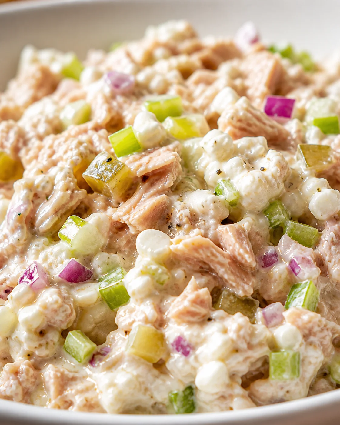 close-up of creamy salmon salad with diced celery, red onion, and pale white chunks in a bowl