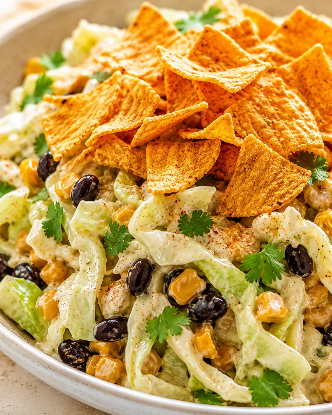 bowl of creamy salad with corn, black beans, lettuce, cilantro, and tortilla chips on top