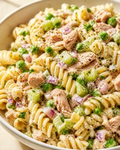 Creamy tuna pasta with peas, celery, and red onion in a white bowl.