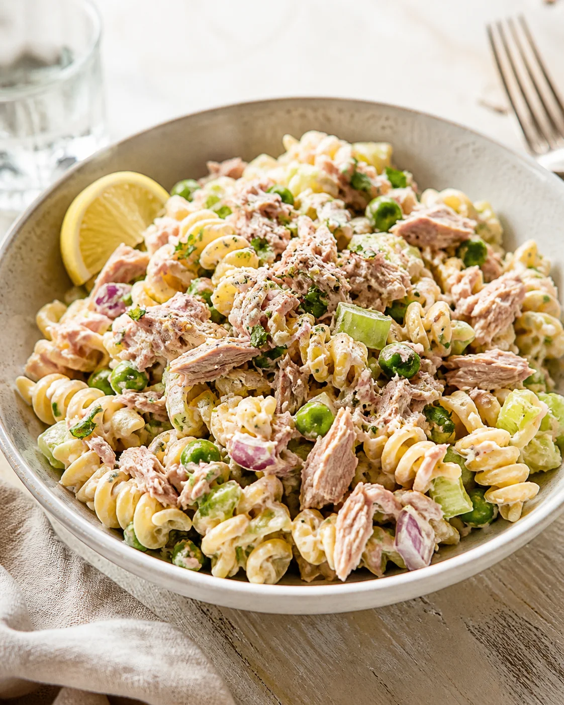 Creamy tuna pasta salad with peas, celery, red onion, lemon wedge.