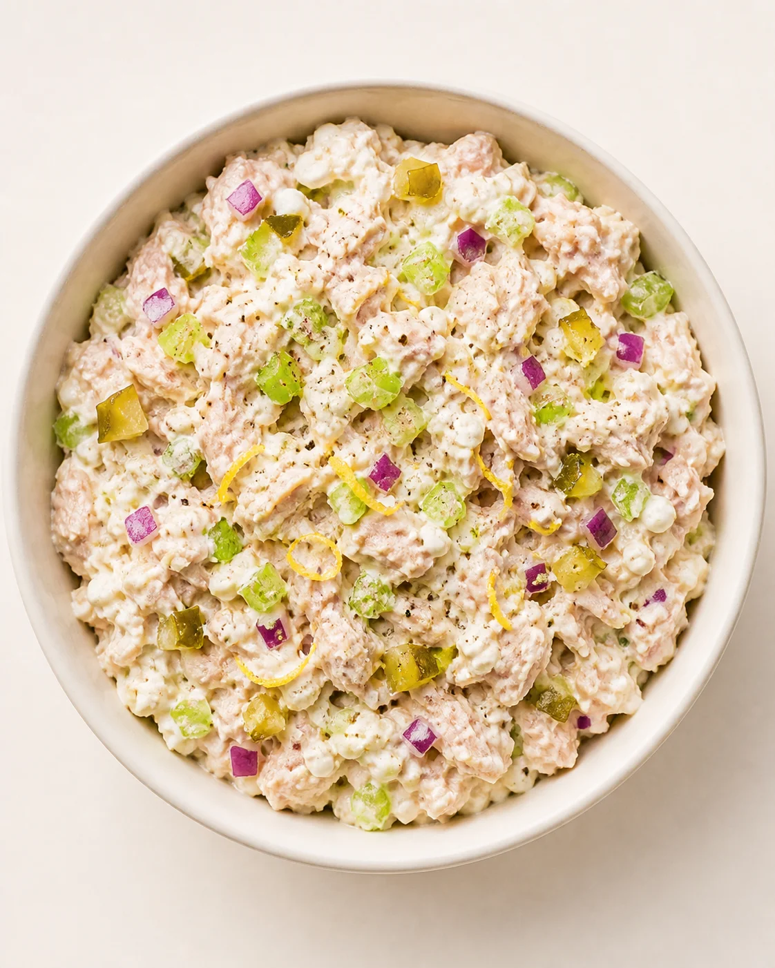 bowl of creamy tuna salad with diced pickles and red onion on a pale background