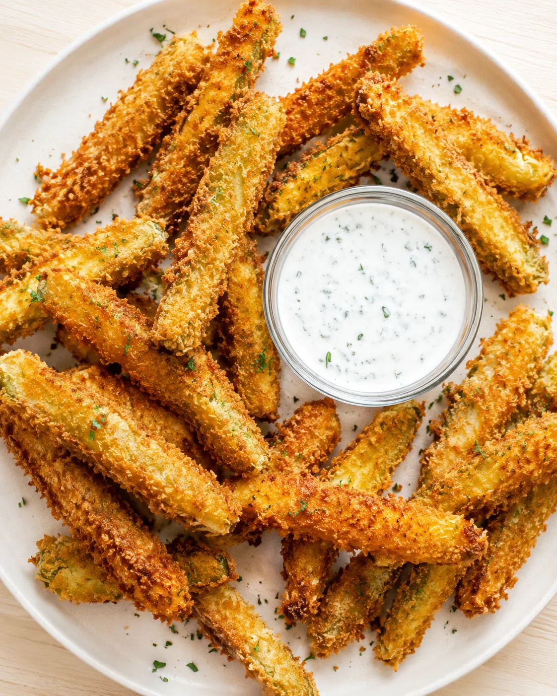 Golden-brown breaded asparagus fries on a white plate with a creamy herb dip in the center.