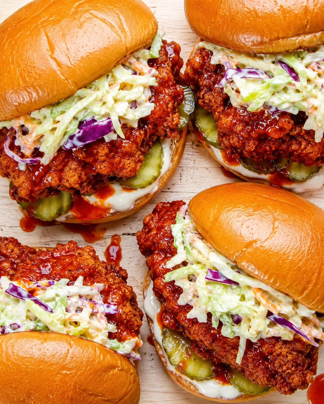 Top-down view of several crispy fried chicken sandwiches with slaw, pickles, and brioche buns.