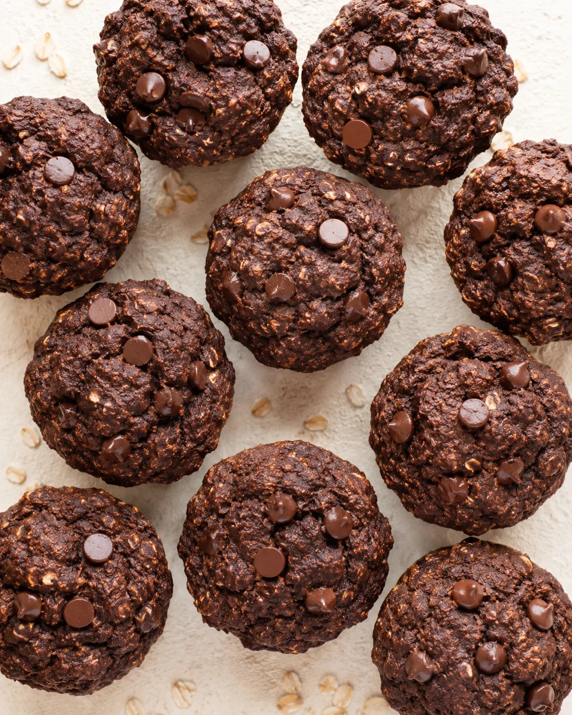 Top-down view of round dark chocolate oatmeal cookies with chips on a light textured surface