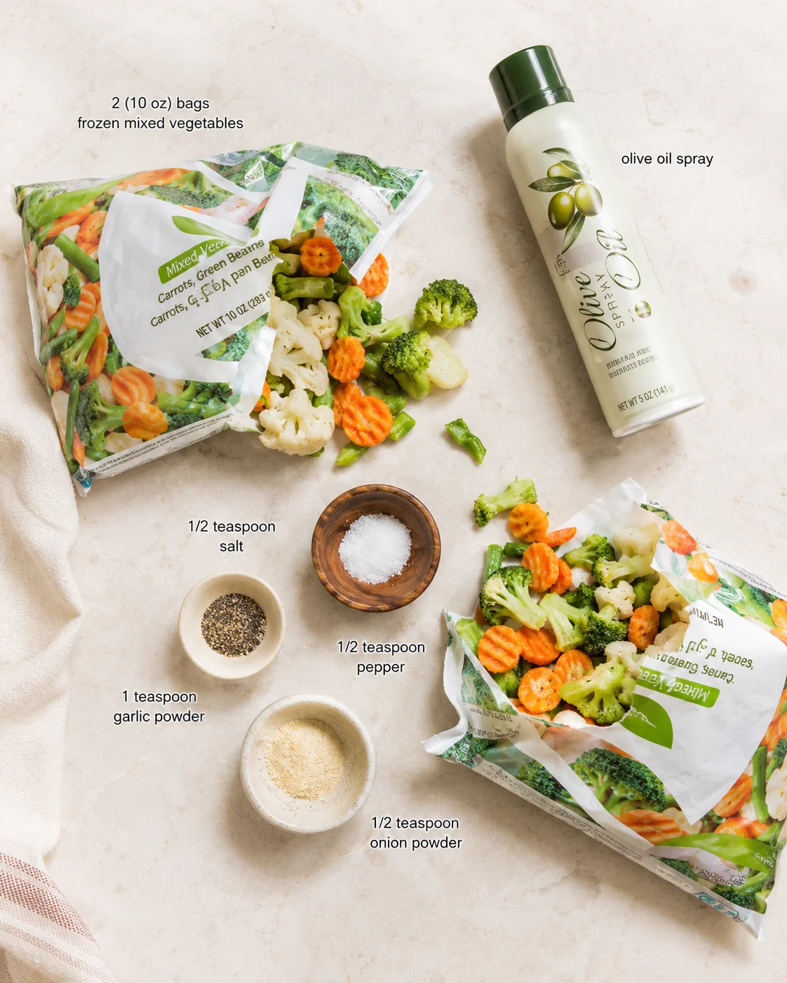 top-down view of frozen mixed-vegetables, olive oil spray, and seasoning bowls on a beige countertop