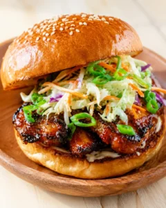 Glassy sesame-seed brioche bun atop a glazed chicken burger with creamy slaw on a wooden plate