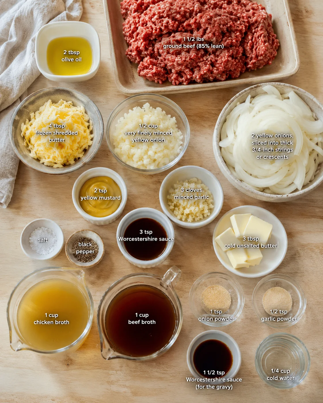 top-down view of a wooden counter with labeled bowls of ground beef and assorted ingredients for cooking.