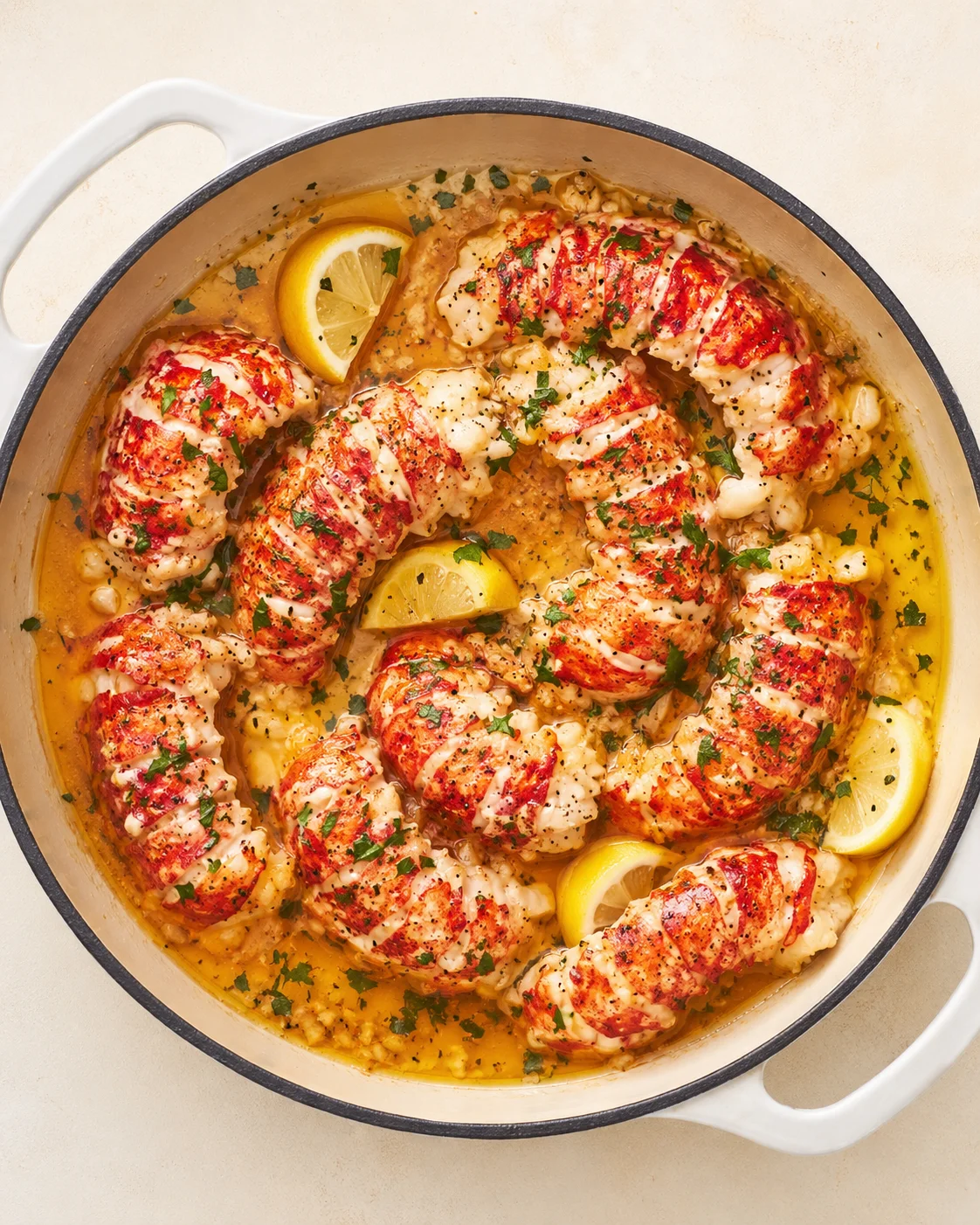 Lobster tails in a creamy lemon-butter sauce, garnished with parsley inside a white enamel Dutch oven.
