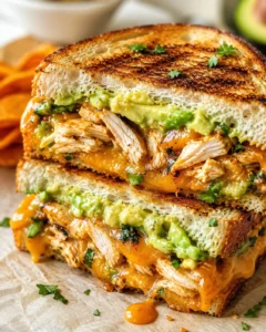 close-up of a thick grilled chicken sandwich with melted cheese and avocado crema on toasted bread